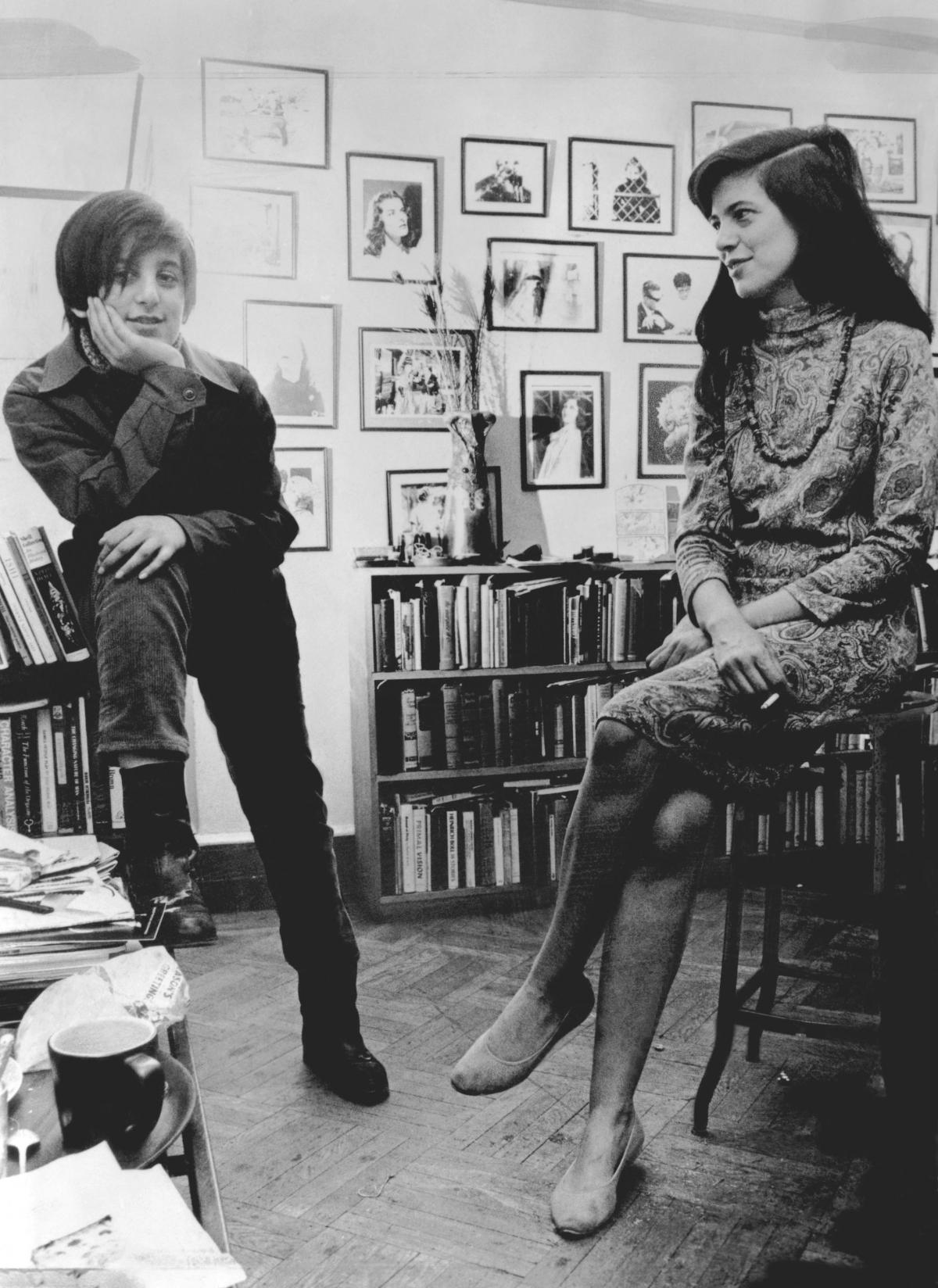 Sontag, seated on a stool, looks at her young son while he rests his hand on his chin