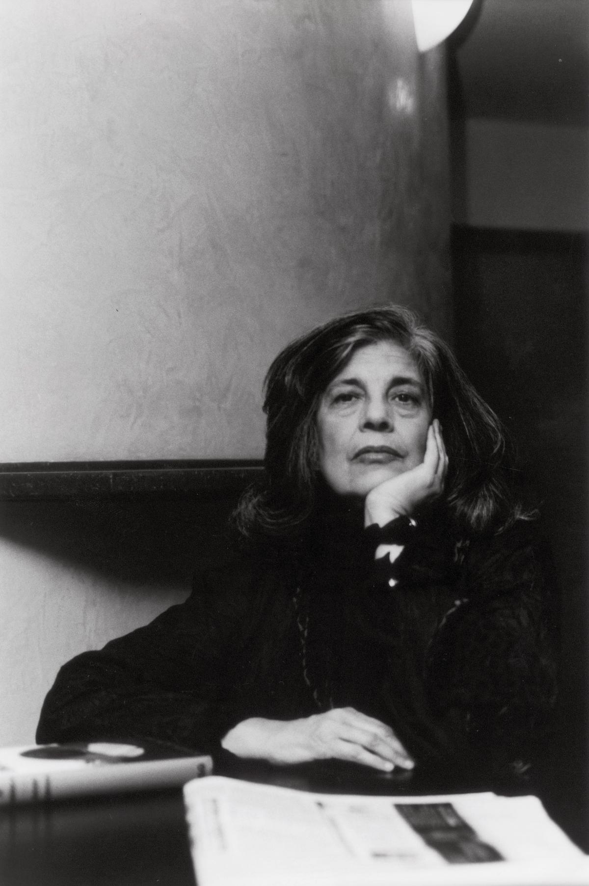 Sontag resting her chin in her hand, seated at a desk
