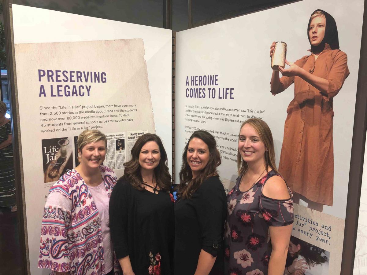 The original three students—Liz, Megan, and Sabring—are joined by Jessica Shleton-Ripper (third from left), who performed many times with Life in a Jar. Here they visit the Irena Sendler exhibit at the Lowell Milken Center for Unsung Heroes in Fort, Scott, Kansas, in 2018. They are standing in front of exhibit walls that say "Preserving A Legacy" and "A Heroine Comes to Life".