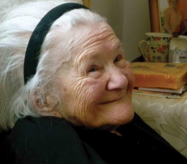 Side portrait of Sendler with books and pots in the background. She is wearing black and a black headband.