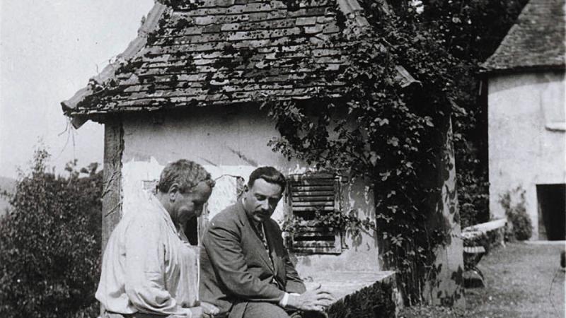 Black and white photo of Gertrude Stein sitting with a male friend on an overlook next to a road.