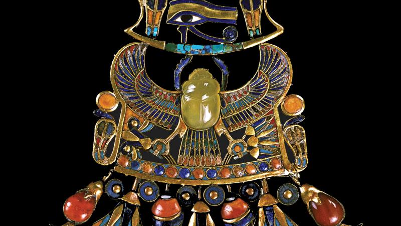 Photo of a golden pectoral body ornament with a yellow-green scarab at its center.