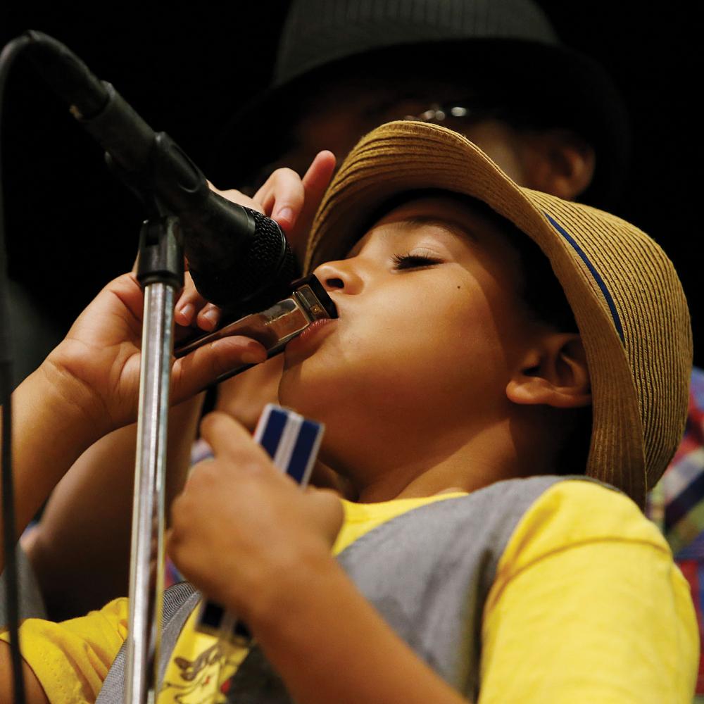 A student plays a harmonica into a microphone during the ABP's program