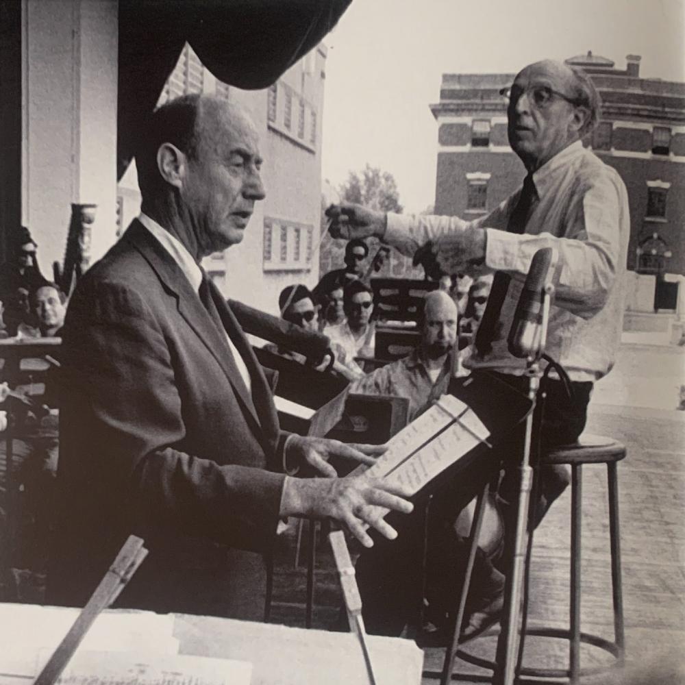 Black and white photo of Copland conducting Lincoln Portrait with Adlai Stevenson at Lewisohn Stadium. 