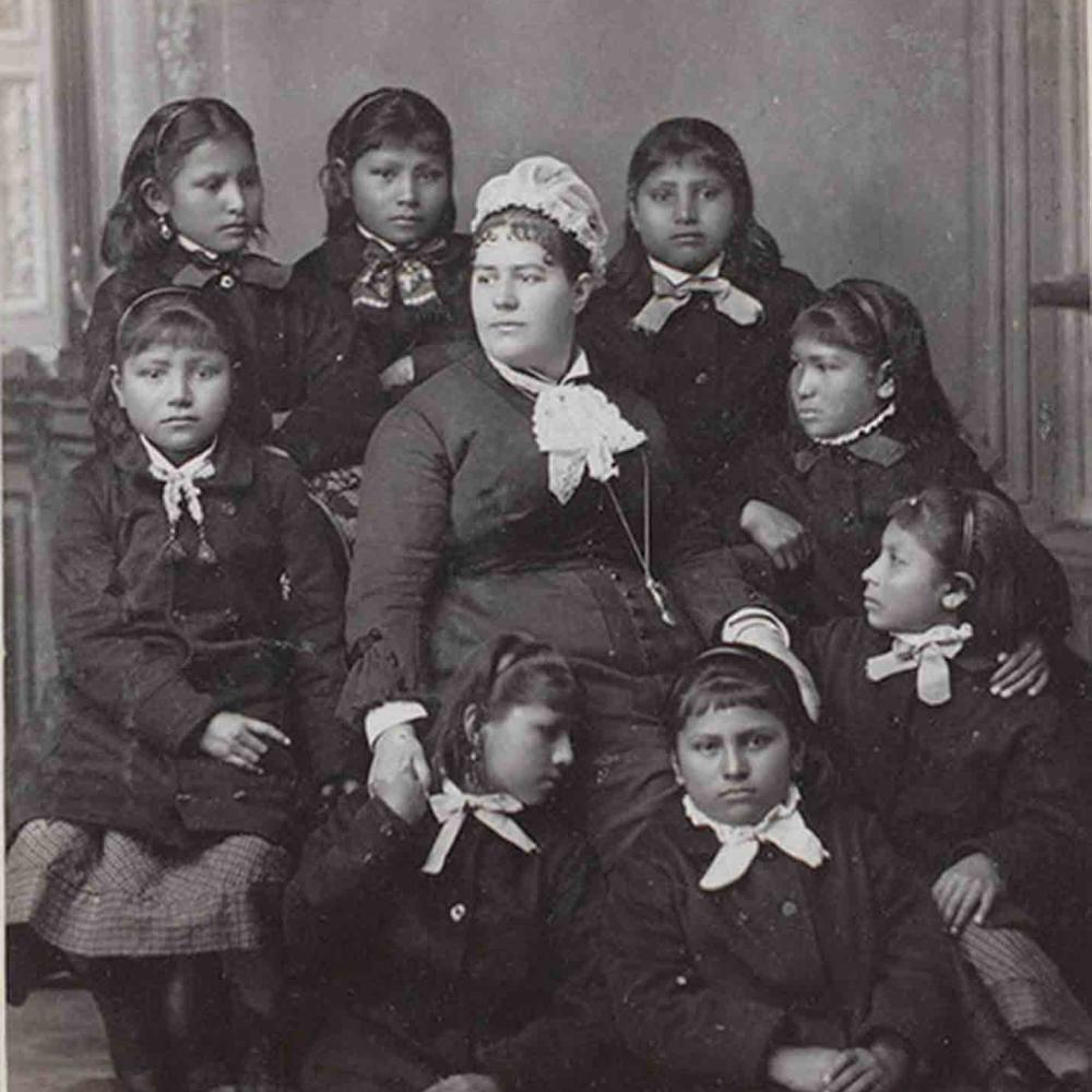 Black and white photo of teacher surrounded by Indian girl students.