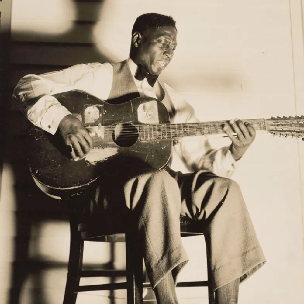 Black-and-white photo of the singer Lead Belly singing and playing the guitar. 