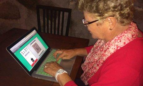 Photo of a woman of an advanced age sitting with an Apple laptop.