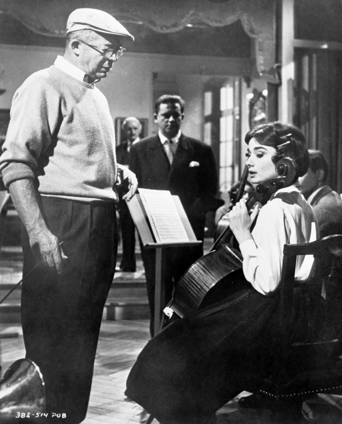 black and white photo of a man standing over a woman sitting playing the cello