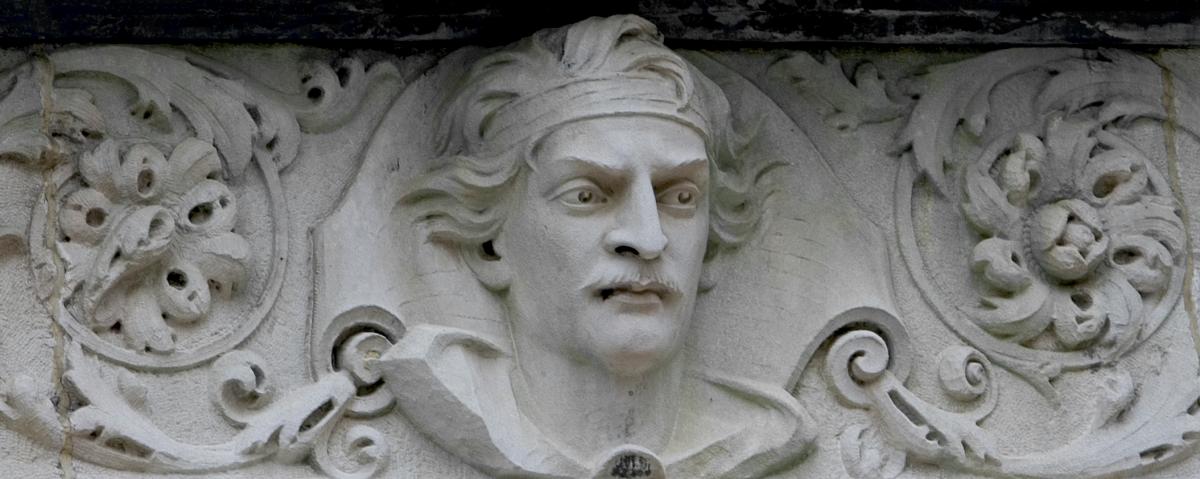 White limestone frieze of Ben-Hur's face, mustachioed and wearing a headband, surrounded by ornamental swirls