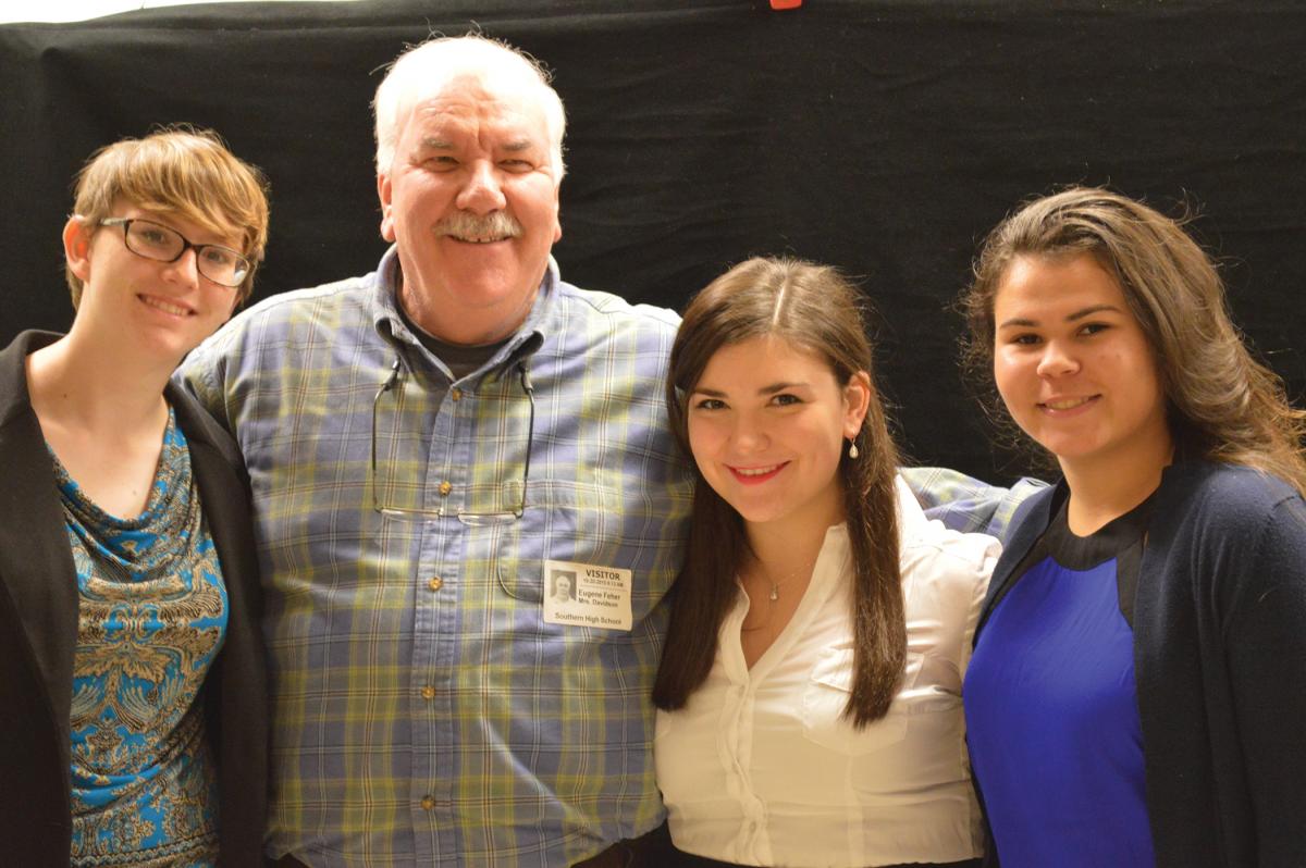 Color photo of Gene Feher posing with several young women on his left and right.