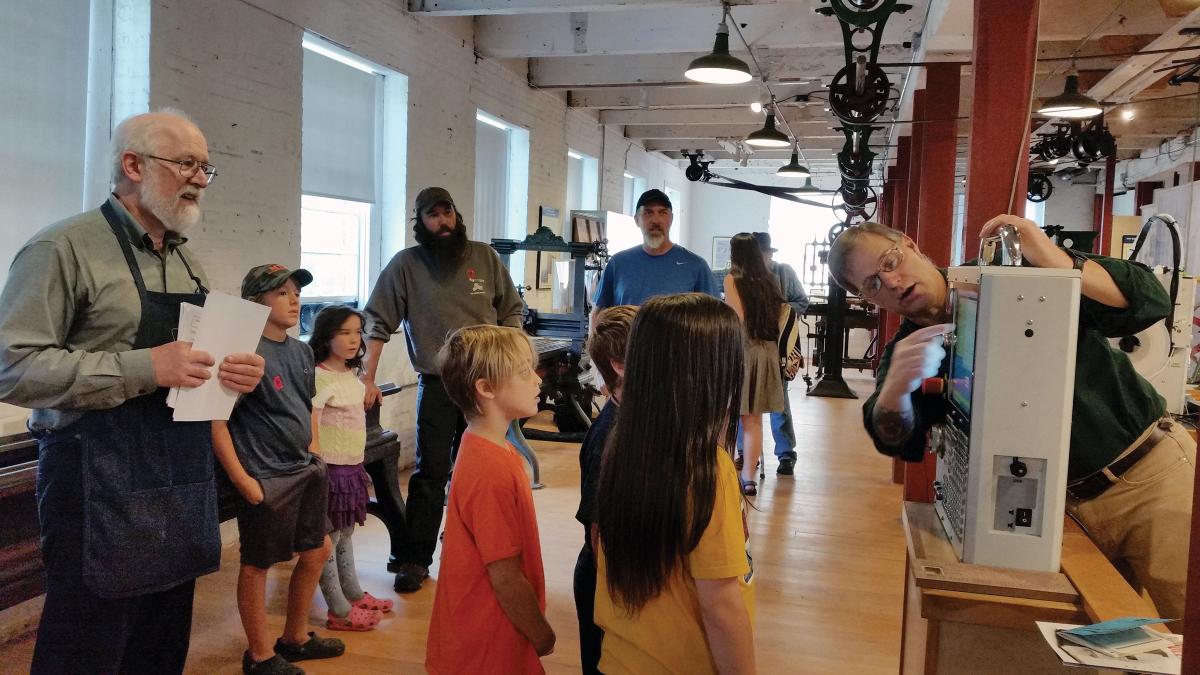 photograph of children standing watching a man operating a machine