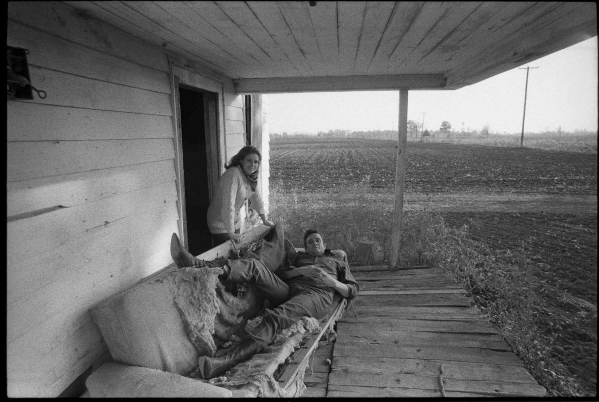 Johnny Cash lying on sofa with June Cash standing next to him.