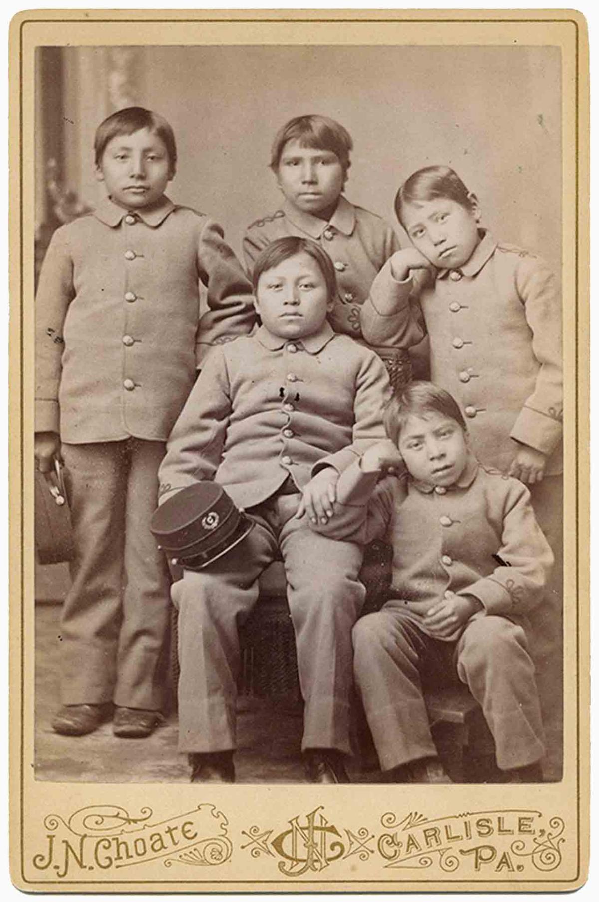 Sepia photograph of 5 young Indian boys in school uniform.