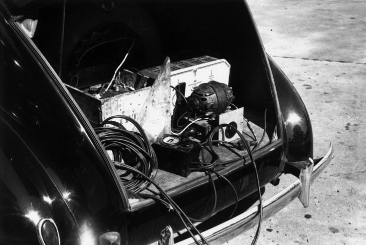 Black and white photo of recording equipment in the trunk of a car.