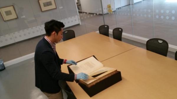 Individual with gloves on examining a large antique book