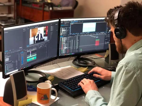 Man sitting at two computers, working on editing video