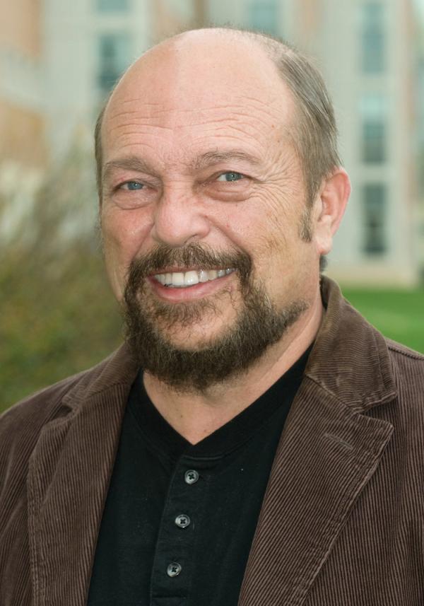 headshot of cartwright, wearing a brown coat and black shirt