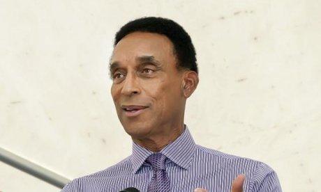 Color photo of an African American smiling in a blue pin-stripe shirt and patterned tie.