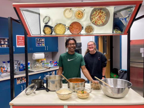 An image of two students cooking with their ingredients reflected in a mirror above them.