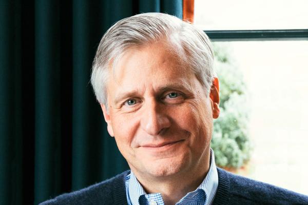 Jon Meacham, silver-haired, standing by a window