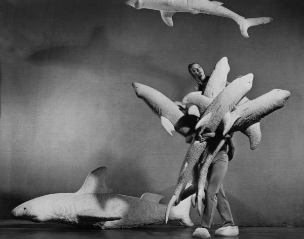 Black-and white-photo of dancer in the show Caviar, peering out above a cluster of stuffed sharks.