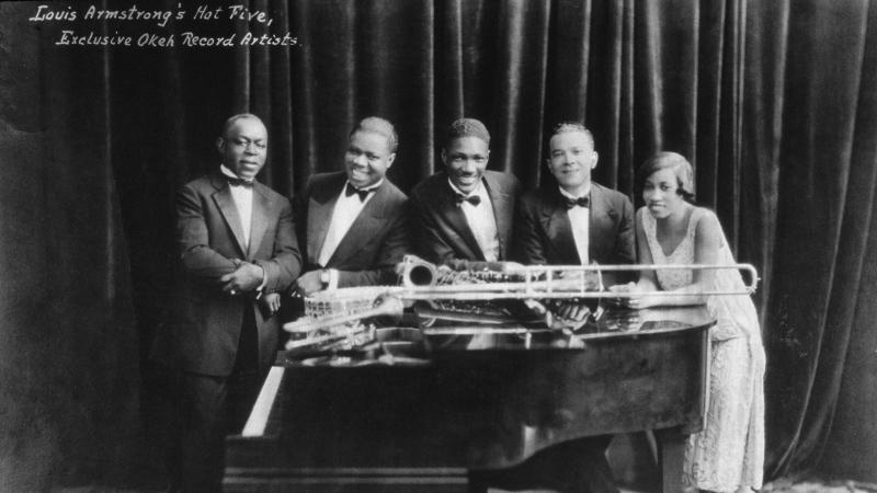 The hot five pose around a grand piano