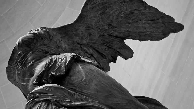 Black and white photo of a winged statue with no head.