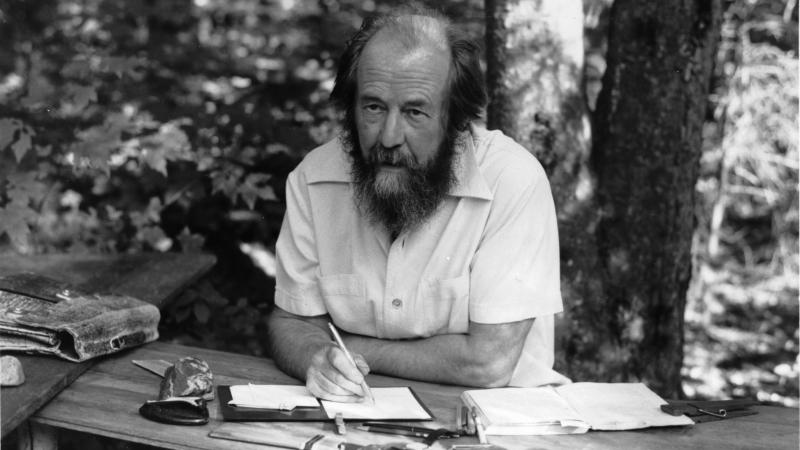 black and white photo of a bearded man writing at a table