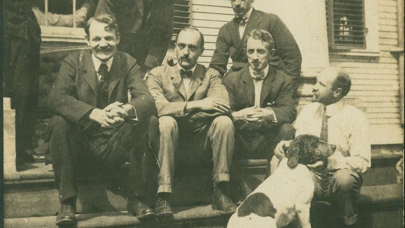 Old photo of six men and a dog sitting on steps