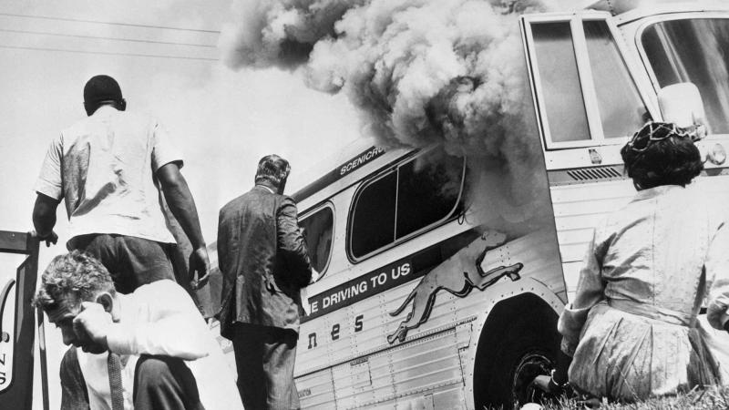 Freedom Riders sit on the ground outside a Greyhound bus after it was set afire by a group of whites who met the group on arrival at Anniston, Ala., on May 14, 1961.