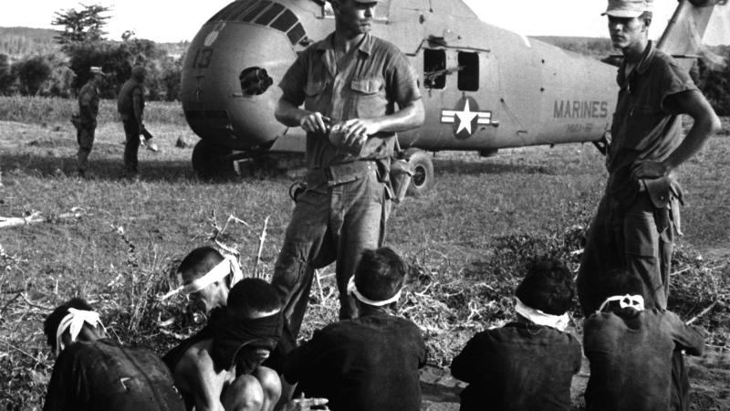 Viet Cong prisoners wait in front of a U.S. Marine Corps Sikorsky UH-34D Seahorse helicopter.