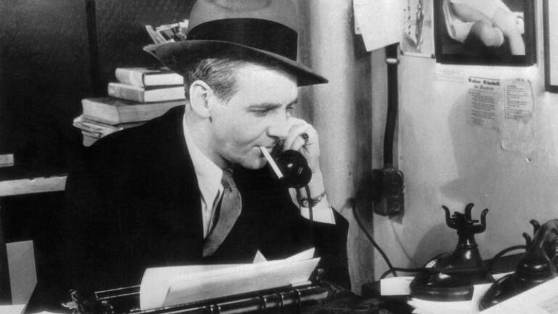 Image of Walter Winchell seated at a typewriter and on the phone