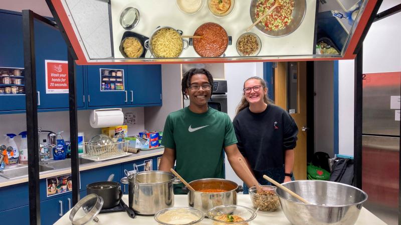 An image of two students cooking with their ingredients reflected in a mirror above them.